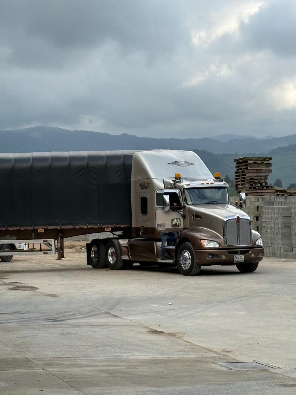 Tractomula Kenworth beige con carpa en zona de montaña